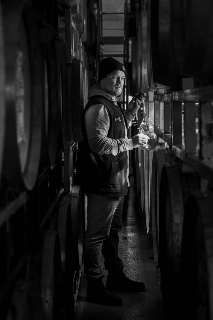 Black and white image of Jackson Holstein, wine grower at Granville Wine Co. sampling wine from a barrel.